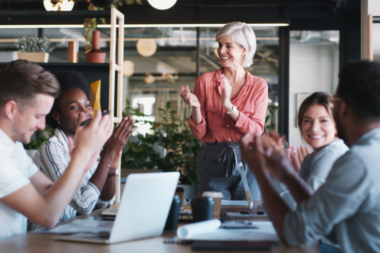 Team applauds a colleague in a modern office, reflecting a positive outlook.