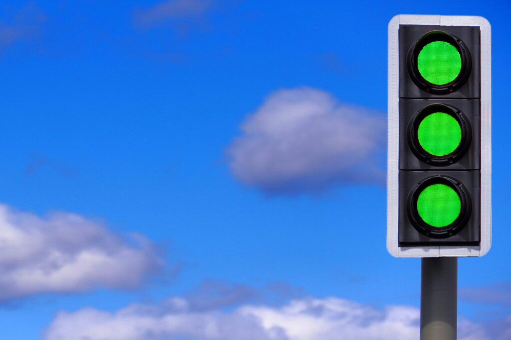 Green traffic light illuminated against a blue sky, symbolizing favorable conditions.